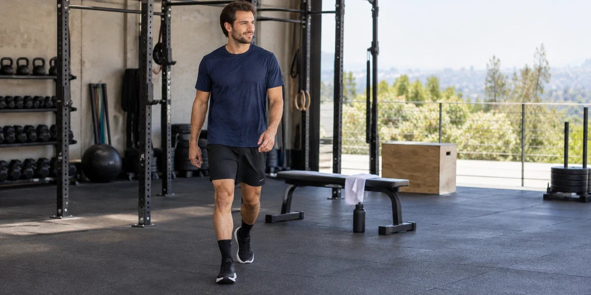 Illustrative gym scene of a man checking movement in mid-thigh workout shorts.